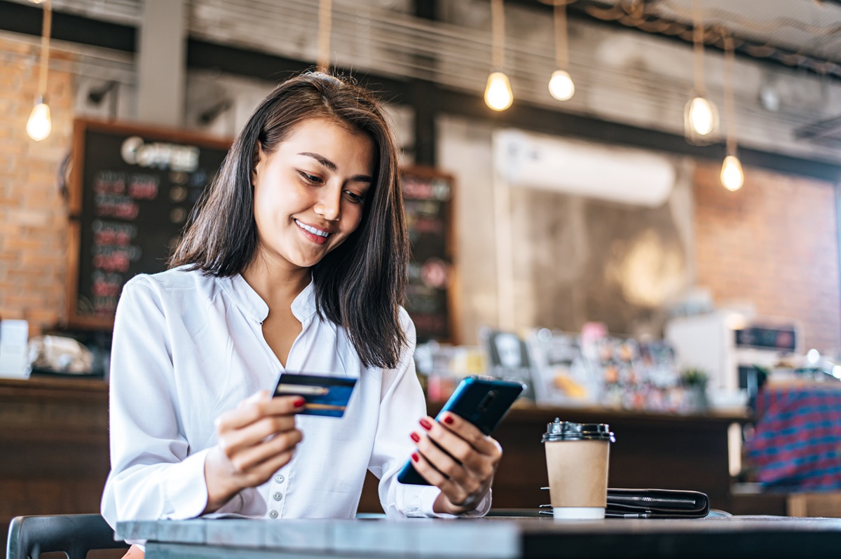 Mujer utiliza una tarjeta bancaria y un teléfono móvil en una cafetería.