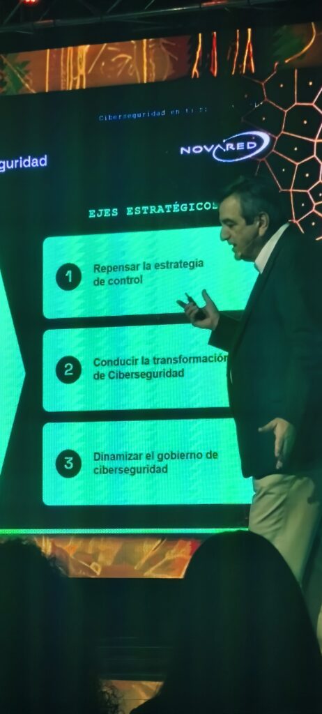 Ciberseguridad e IA — expositor ante diapositiva de Novared con tres ejes